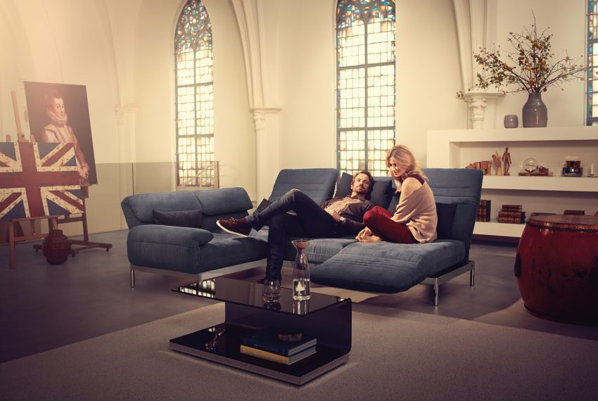 Zwei Personen auf einem Rolf Benz Plura Sofa mit passendem Couchtisch